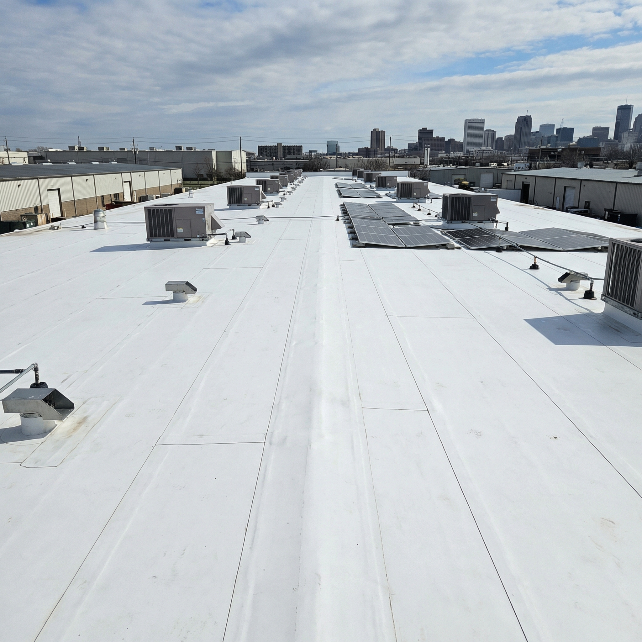Wide white commercial TPO roof with rooftop units and solar panels